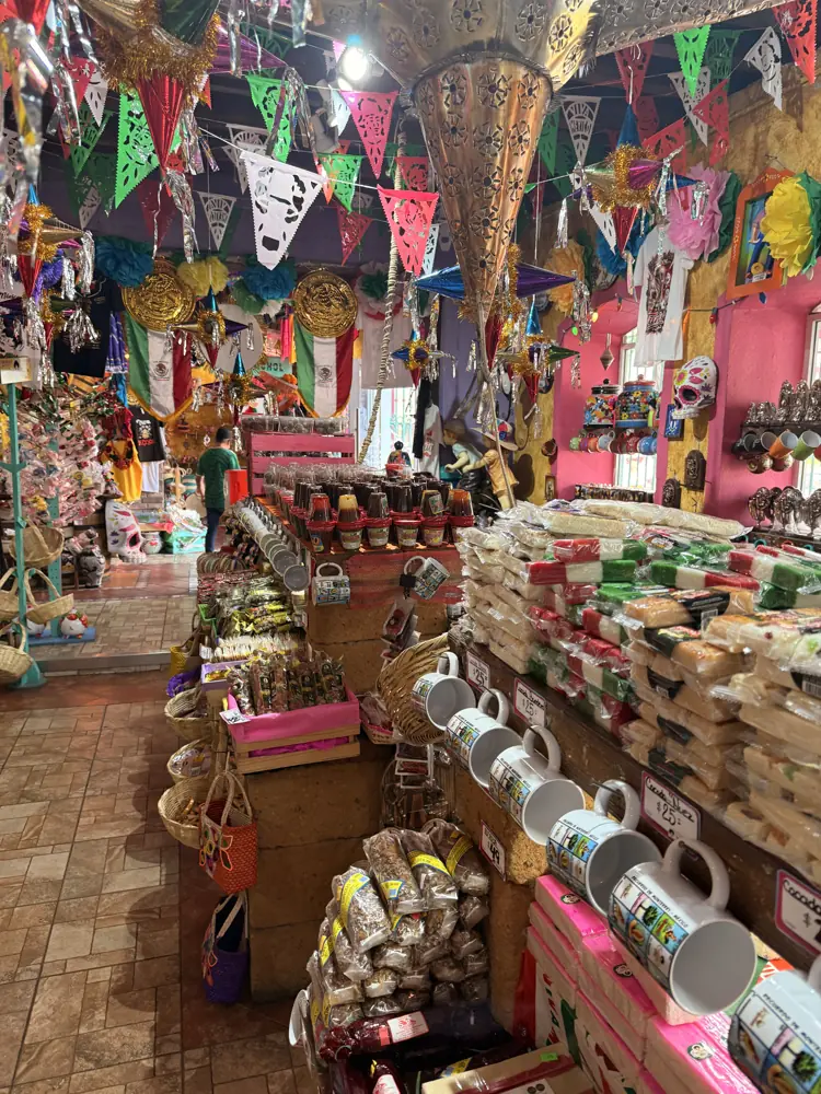 Pasillo del local con papel picado y banderines colgados del techo, mesas de artesanía y tazas a los lados