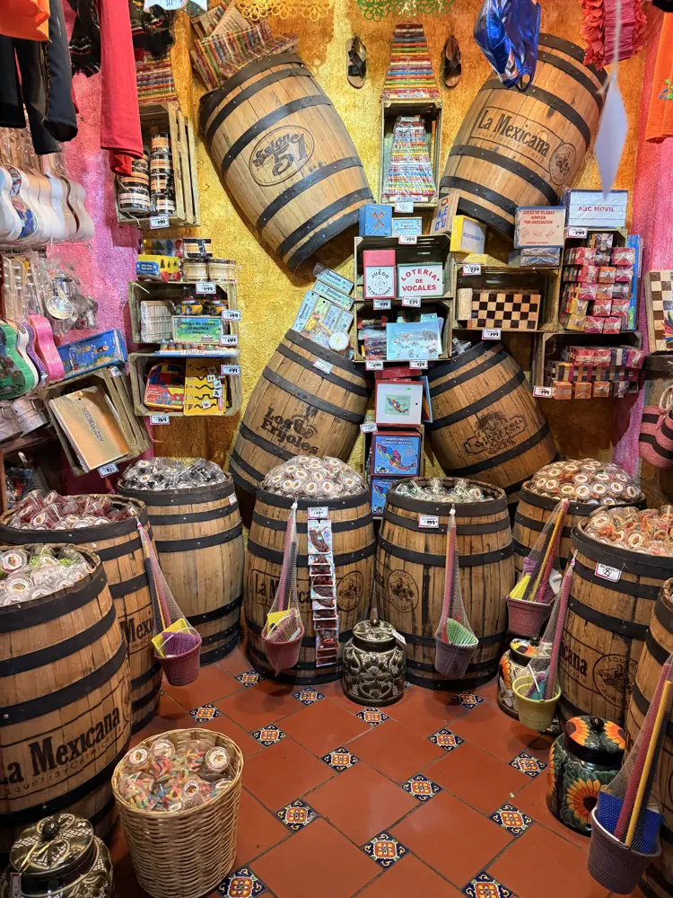 Barriles de madera con dulce a granel sobre piso de mosaico rojo, con frascos y canastas alrededor