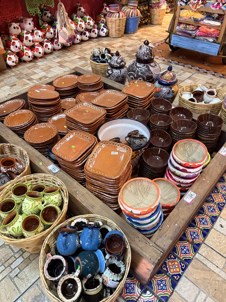 Cazuelas y platos de barro apilados por tamaño junto a tazas y piezas de talavera