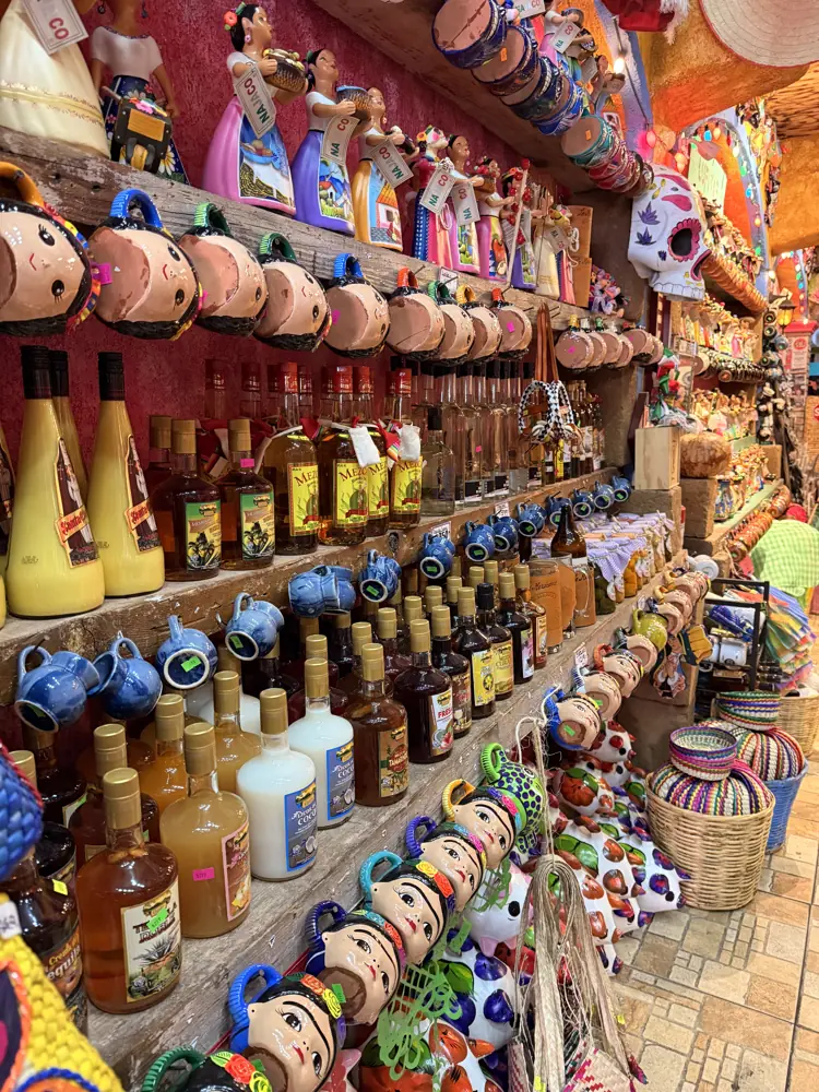 Muro de estantes con botellas, alcancías de cerdito y piezas de talavera de piso a techo