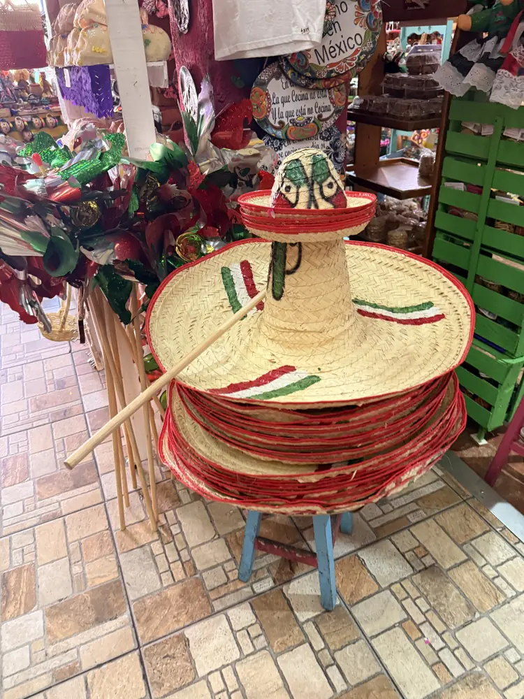Torre de sombreros de palma bordados en verde, blanco y rojo sobre un banco de madera
