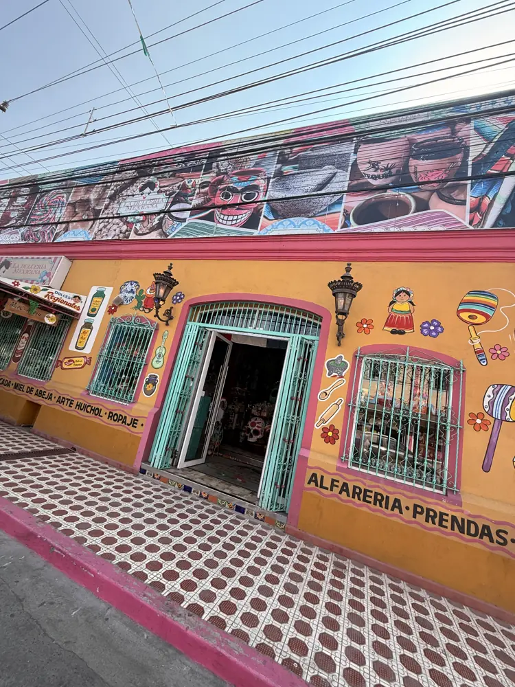 Fachada de La Dulcería Mexicana pintada de naranja con murales, reja verde y el letrero Alfarería Prendas