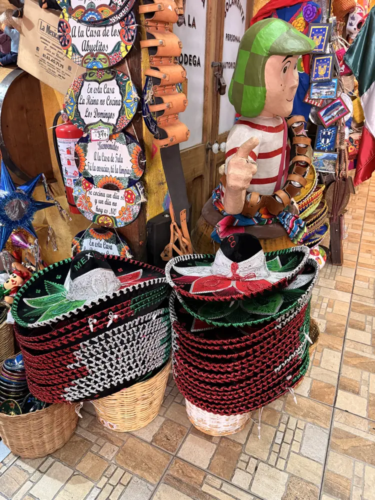 Canastas tejidas en rojo y negro junto a jícaras y objetos de palma, bajo carteles de madera rotulados